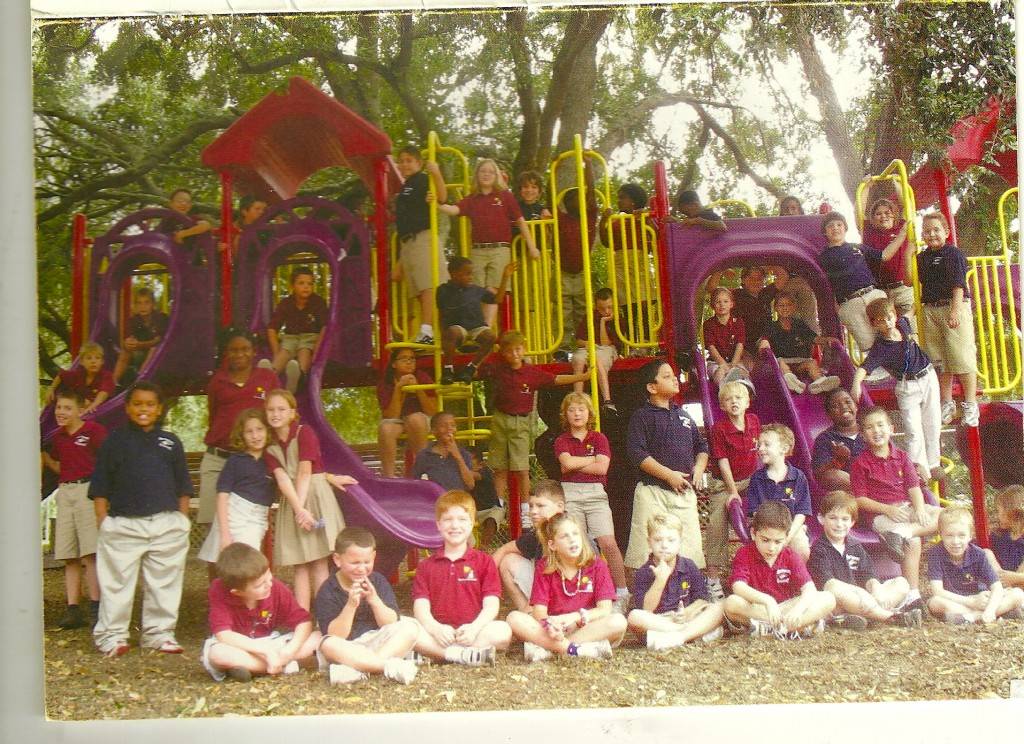Kids in maroon shirts and blue shirts with khaki bottoms on yellow and maroon playground equipment