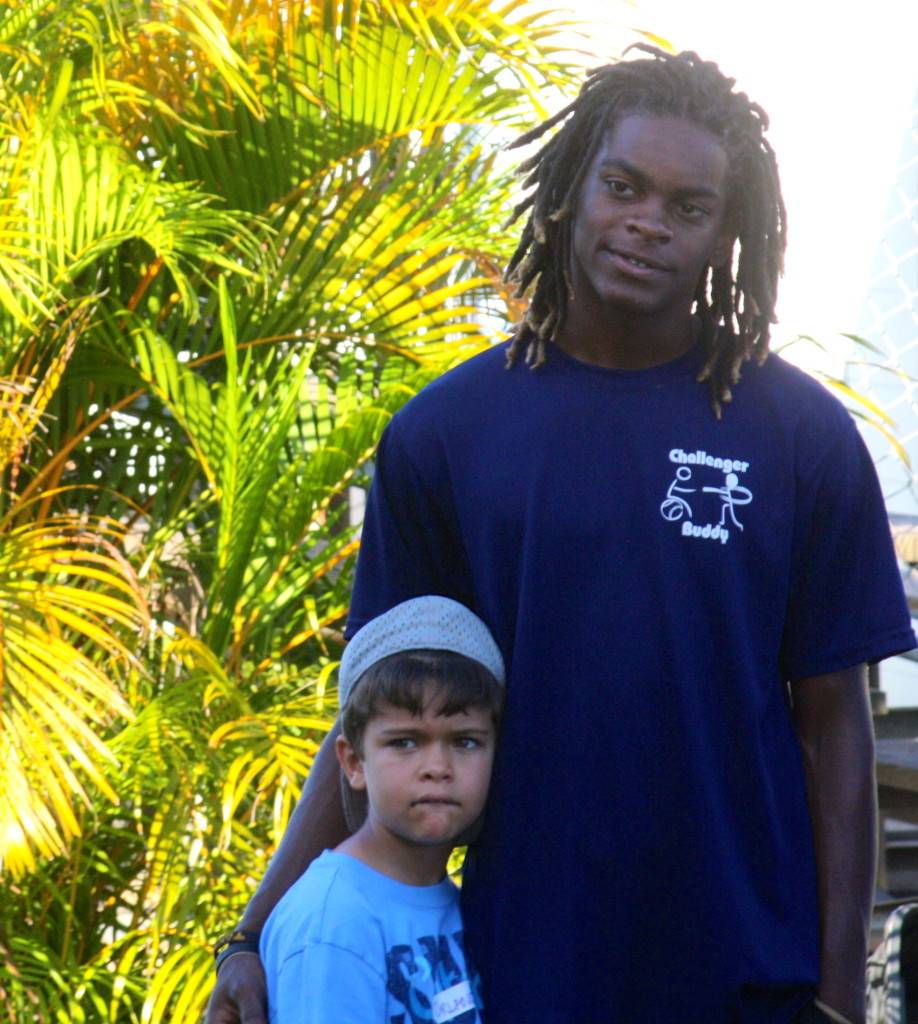 Picture of a young boy wearing a tshirt and baseball cap standing with a young man wearing a tshirt