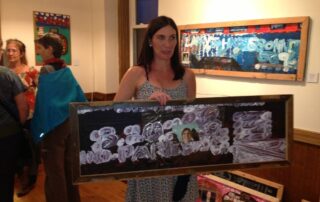 Woman with brown hair and white skin holding a painting by Larry Bissonette.