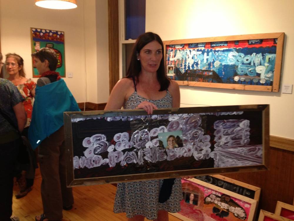 Woman with brown hair and white skin holding a painting by Larry Bissonette.