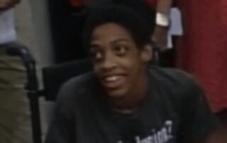 Teenager with brown skin and dark brown hair smiling and wearing a "got inclusion" t-shirt.