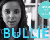Image description black and white photo of girl with long brown hair looking at the camera . blue text reads"BULLIED" and NOT in background. Upper right hand corner of image has green circle with with white text that reads "spread the word"