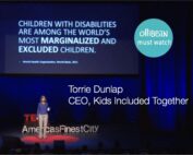 A photograph of a woman wearing a purple shirt and khaki pants giving a speech on stage. TED in bold red letters , and "America's Finest City" is partially visible behind her. On a large screen behind her " Children with disabilities are among the world's most marginalized and excluded children." To the right there is a turqoise circle with white font "Ollibean Must Watch"/ Also in white font " Torrie Dunlap, CEO, Kids Included Together