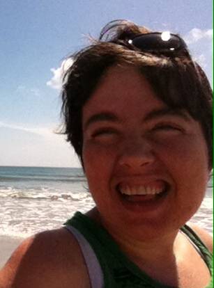 Photograph of Amy Sequenzia, woman with white skin and dark brown hair smiling at the camera at the beach.