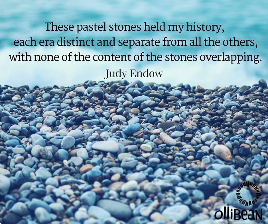 Photograph of stones on a beach. Text reads " hese pastel stones held my history, each era distinct and separate from all the others, with none of the content of the stones overlapping. Judy Endow on Ollibean.